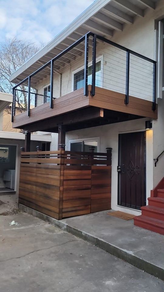 A brown wooden deck with a black railing sits above a matching wooden privacy fence next to a building's entrance.