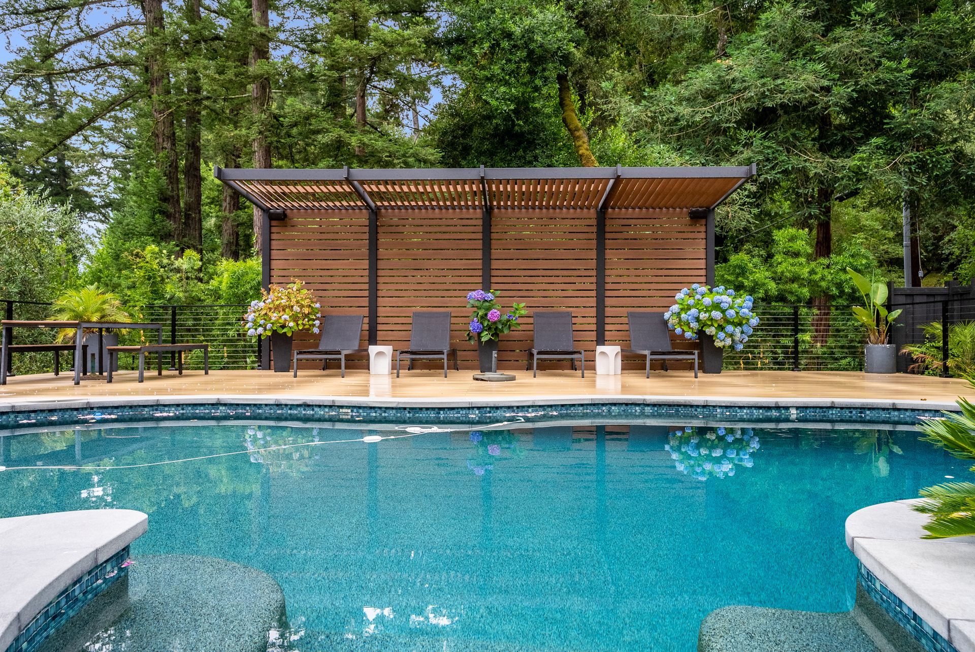 Backyard pool with a wooden cabana, lounge chairs, and trees surrounding the deck
