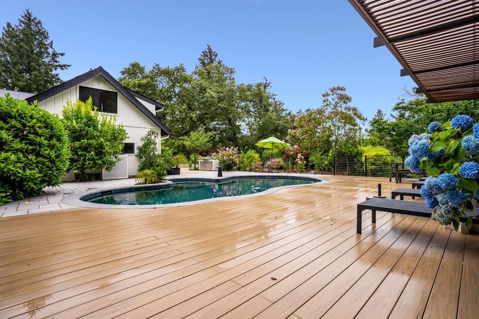 Backyard deck with a swimming pool, lounge chair, and blue hydrangeas beside a house
