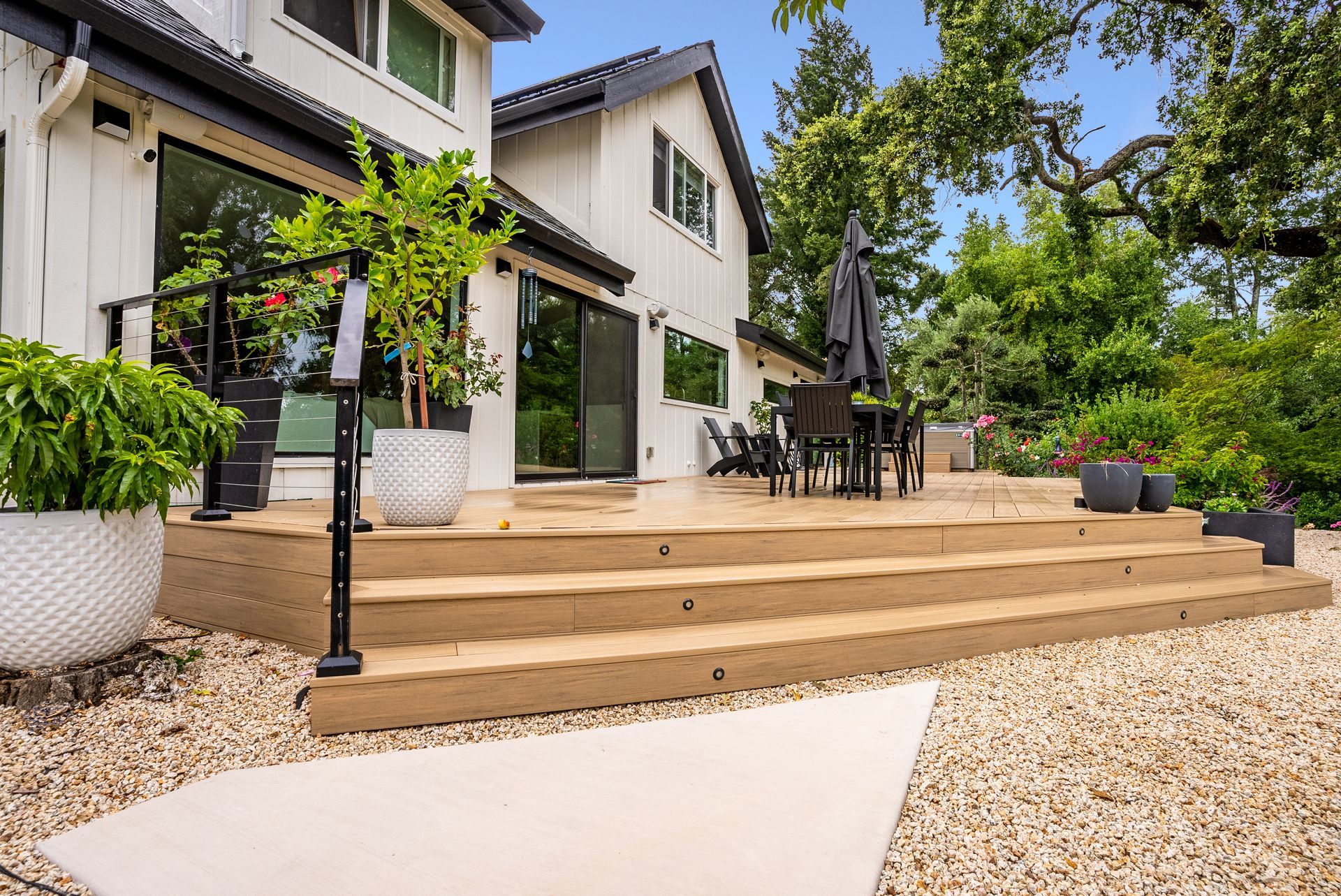 Modern house patio with wooden steps, white planters, and outdoor seating in a sunny garden