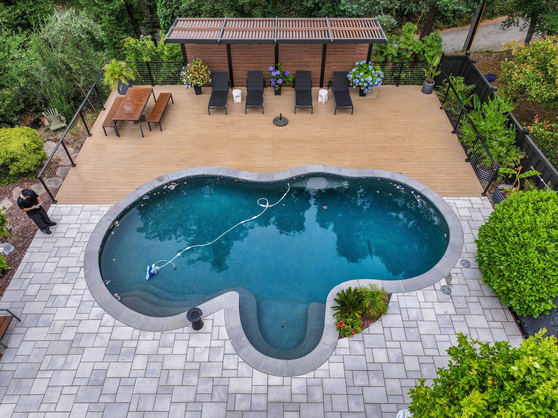Backyard pool with stone patio, wooden deck, lounge chairs, and pergola seating area