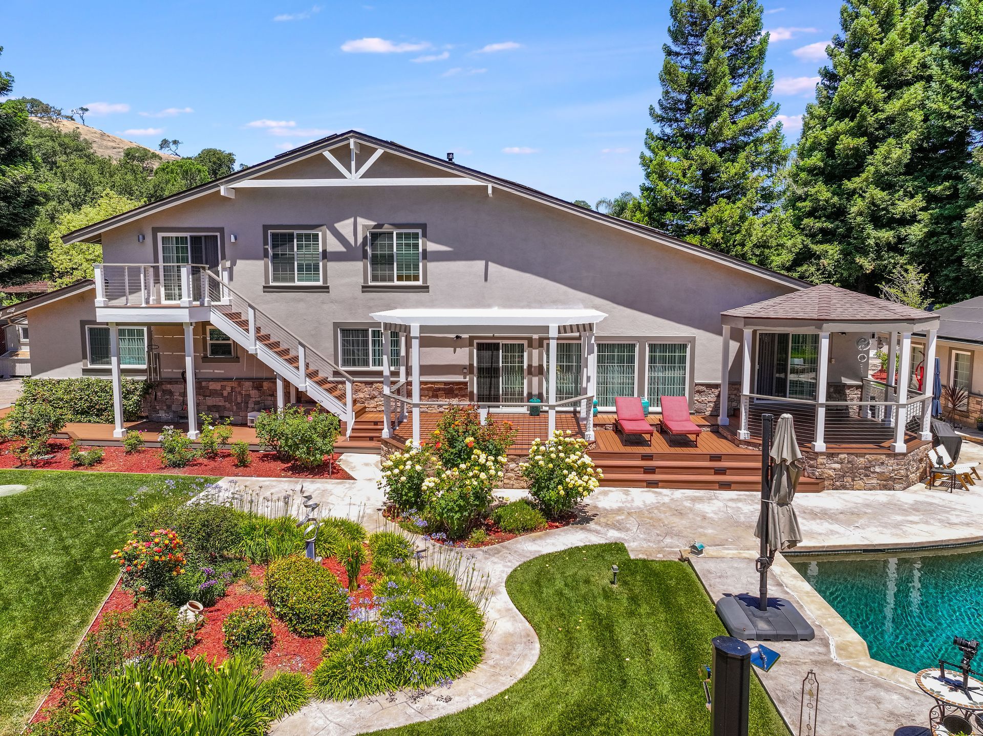 Sunlit stucco house with tiled roof, palm trees, and a wide paved driveway under a clear blue sky