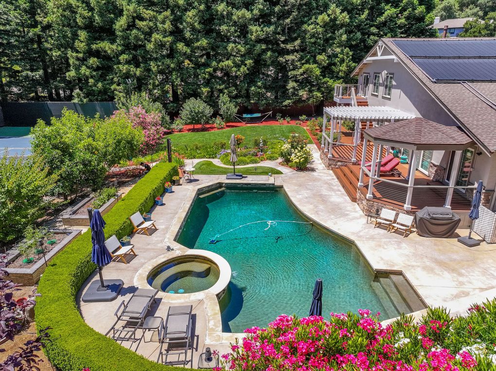 Backyard pool with hot tub, patio lounge chairs, and a house surrounded by lush greenery and pink flowers