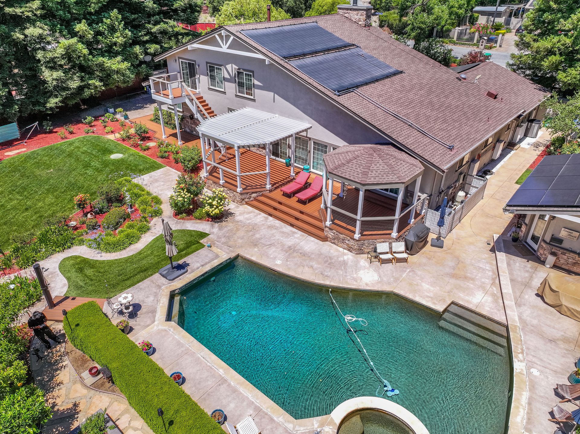 Aerial view of a house with a backyard pool, patio, garden, and solar panels on the roof