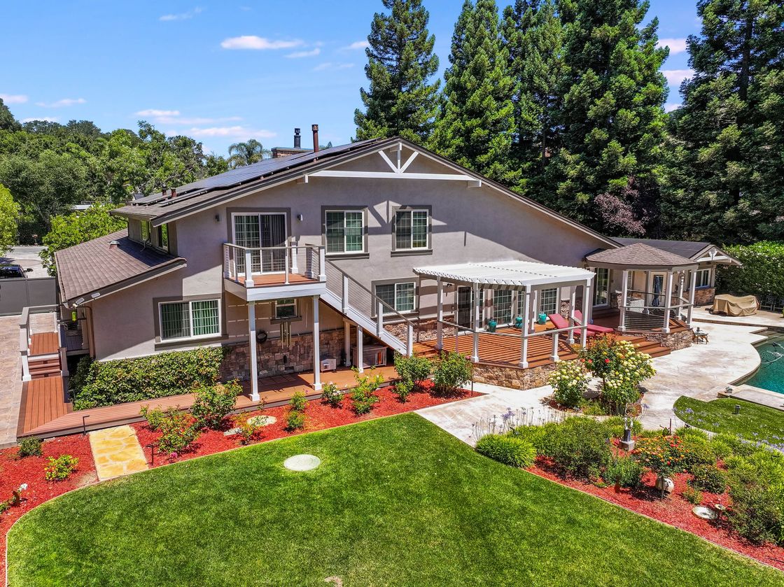 Two-story house with deck, landscaped front yard, and curved walkway under a blue sky