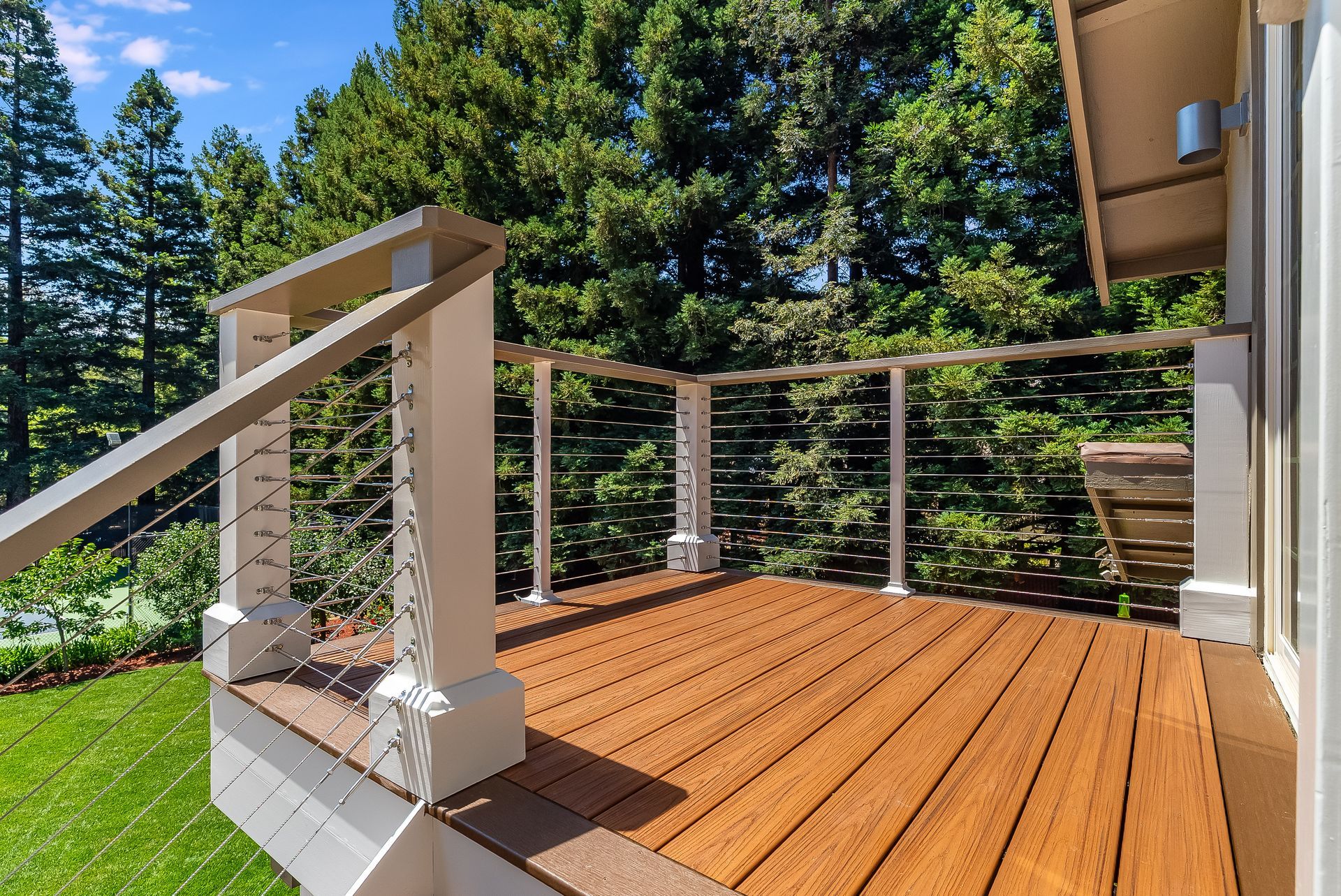 Wooden deck with white railing and evergreen trees in bright sunlight
