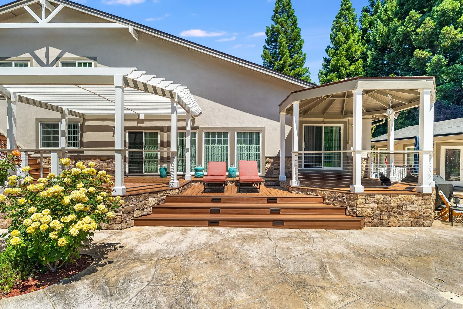 Backyard patio with wooden deck, pergola, outdoor seating, and a house exterior on a sunny day