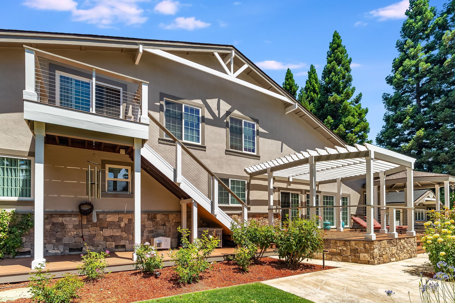Two-story beige house with covered porch, white railings, and landscaped front yard under a blue sky