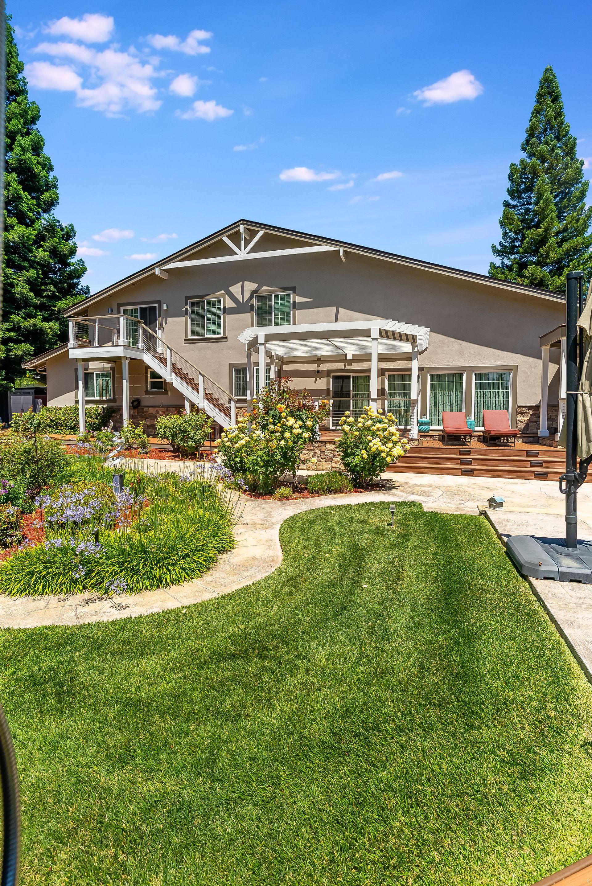 Large house with landscaped garden, curved stone path, and patio under a bright blue sky