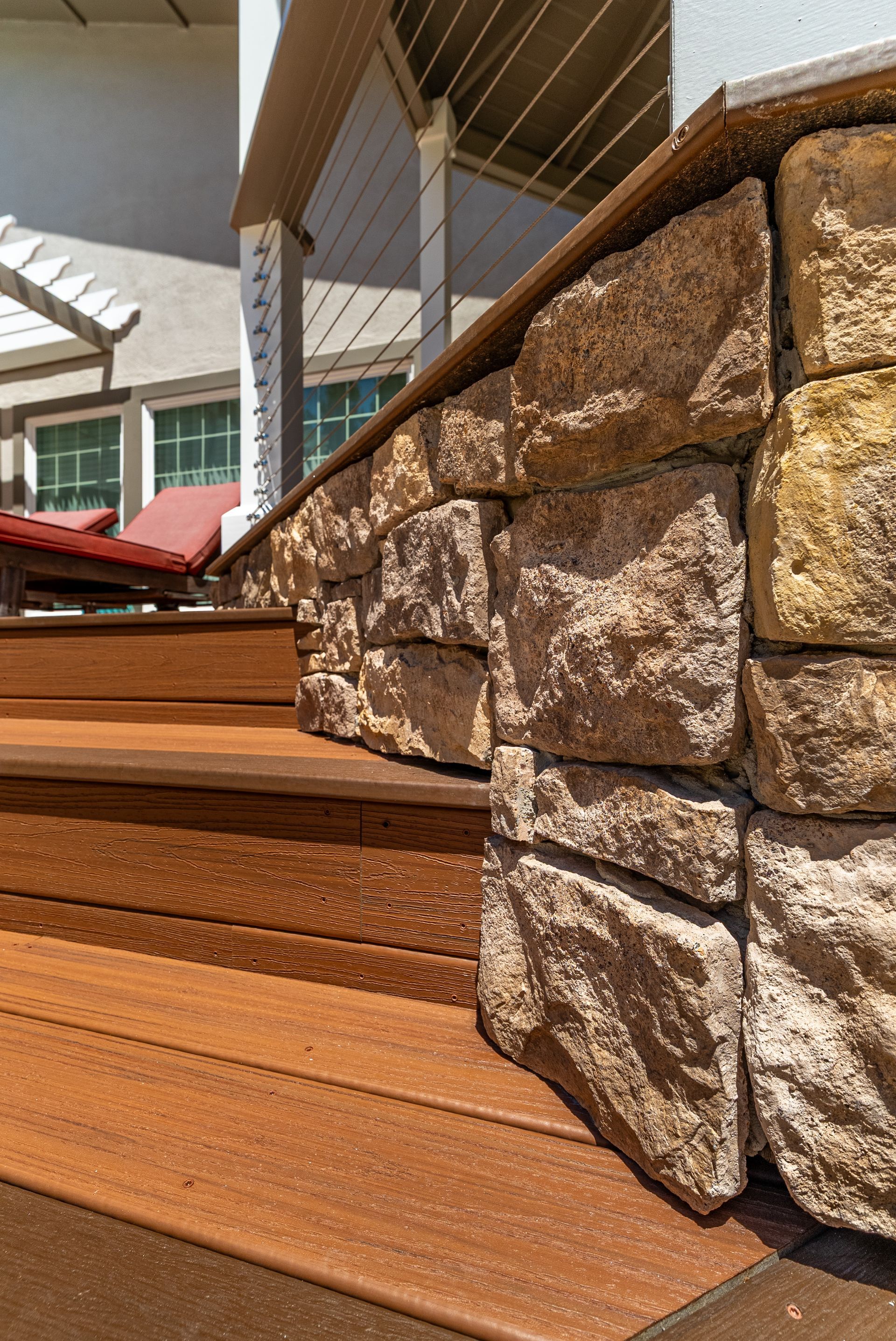 Stone retaining wall beside wooden steps and a deck railing outdoors