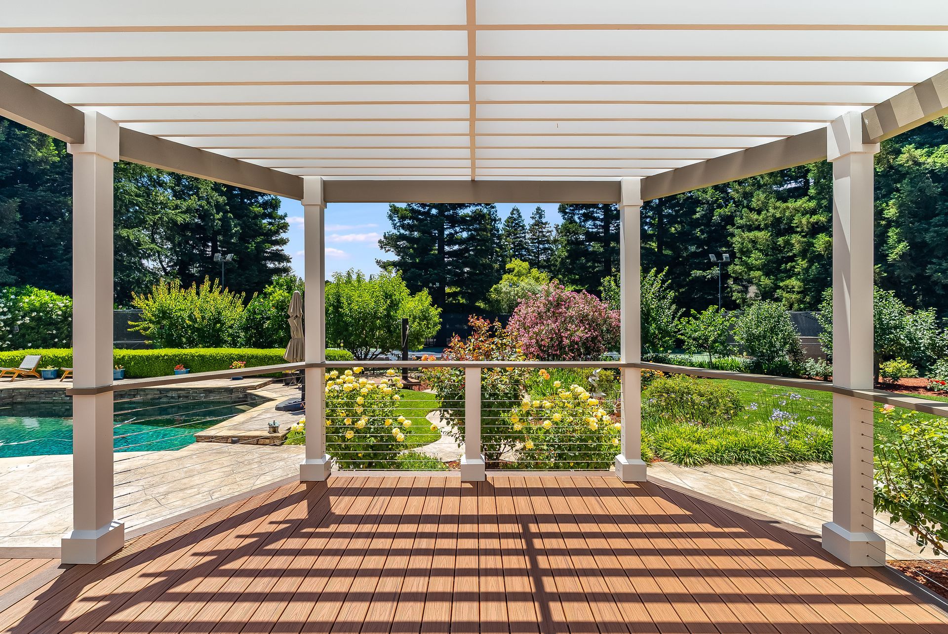 Covered patio with white columns, wooden deck, and a garden view beyond the railing.