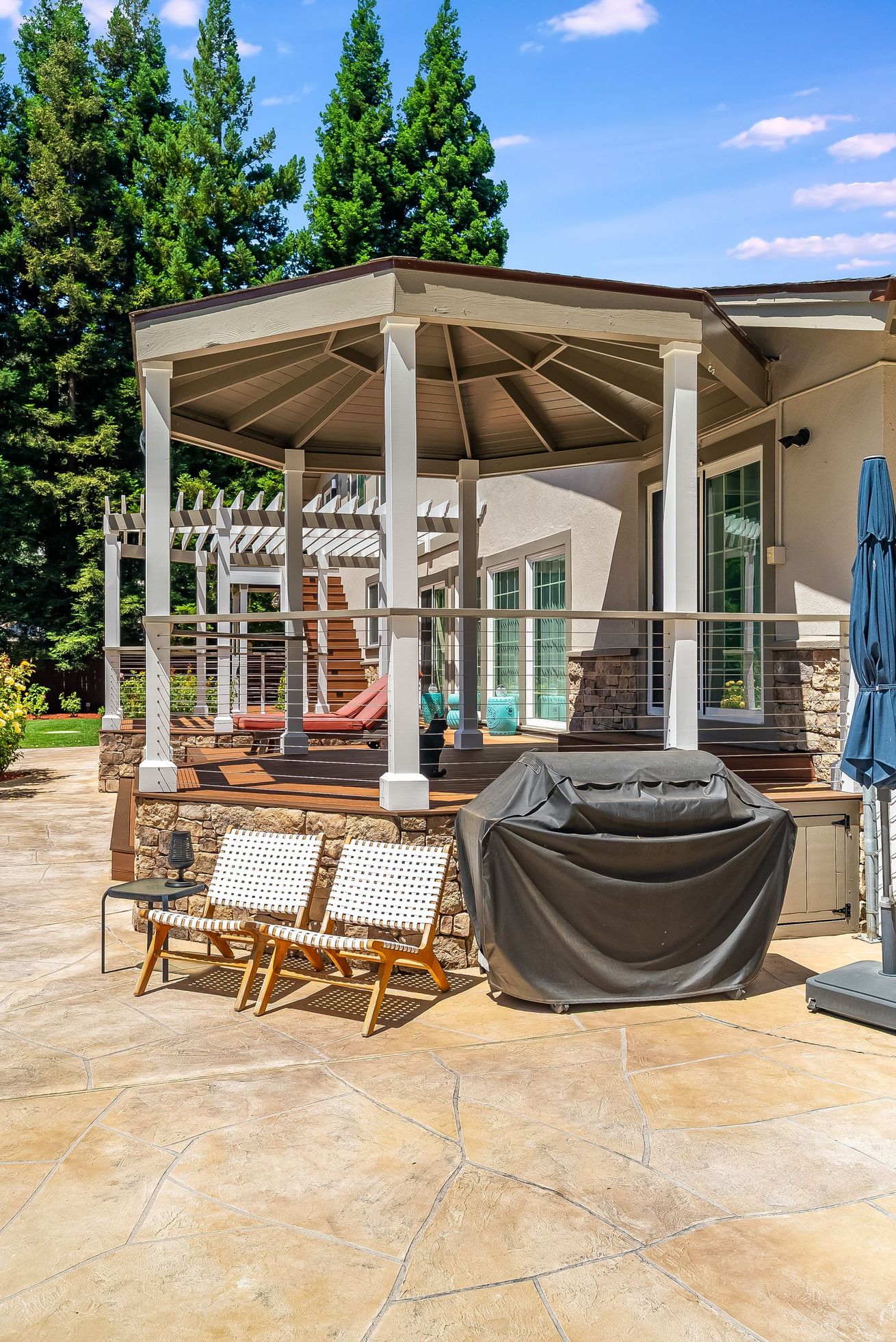 Patio with white gazebo, outdoor chairs, grill, and trees in a sunny backyard
