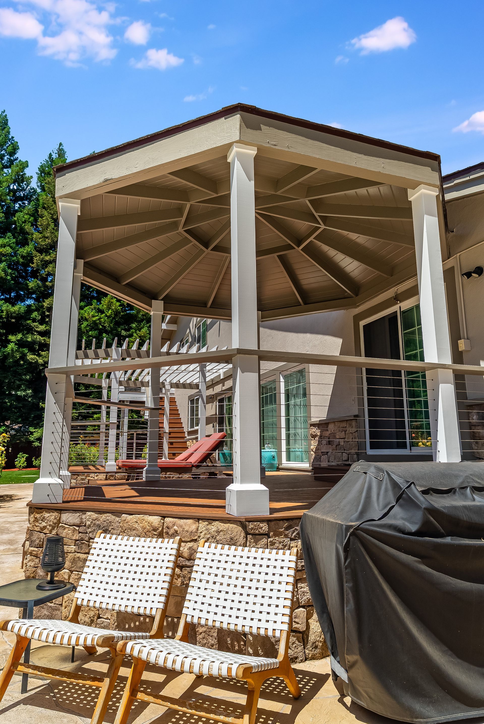 Outdoor pavilion under construction with white columns, wooden roof, and covered furniture in front