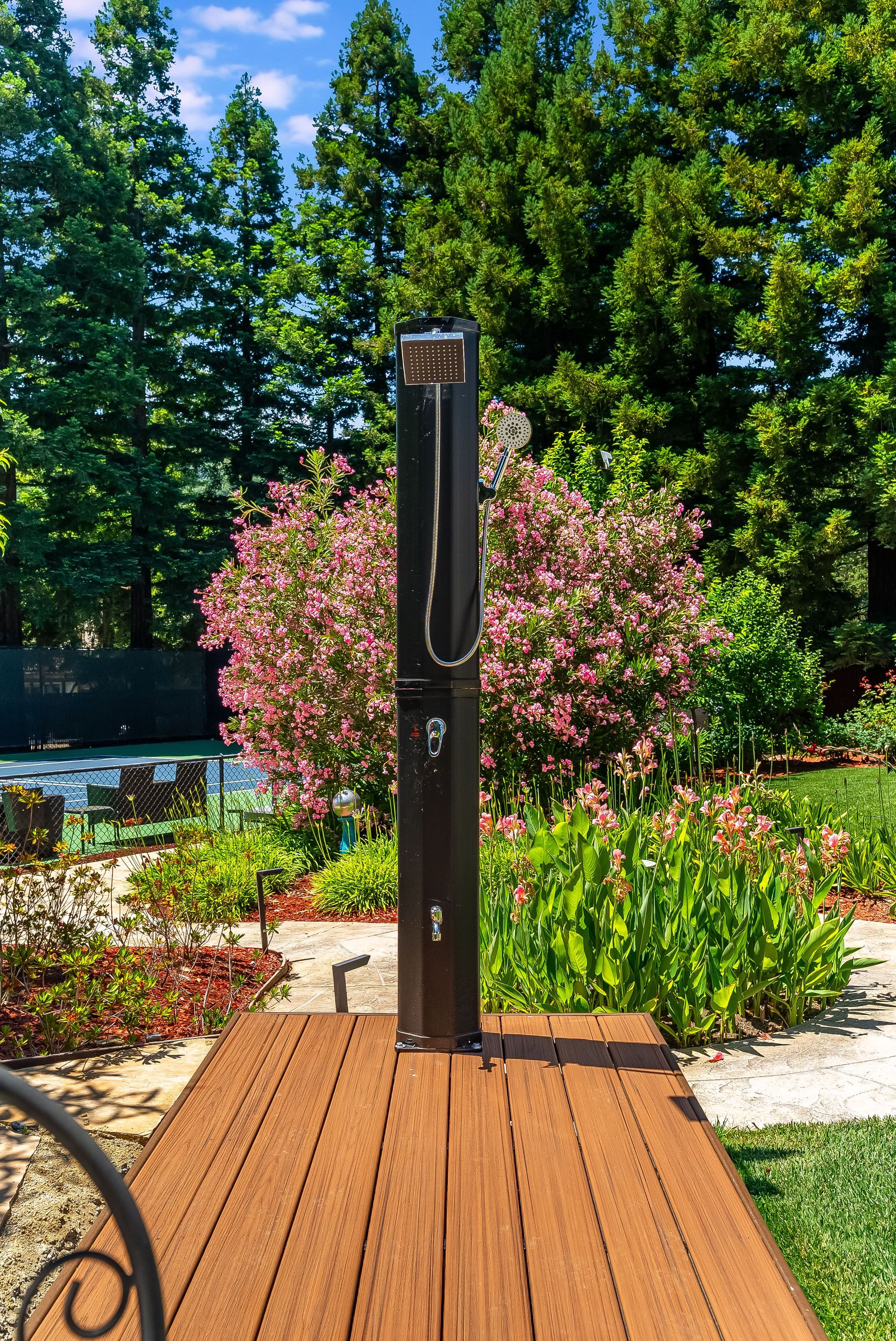 Outdoor shower on a wooden deck in a landscaped garden with flowers and trees