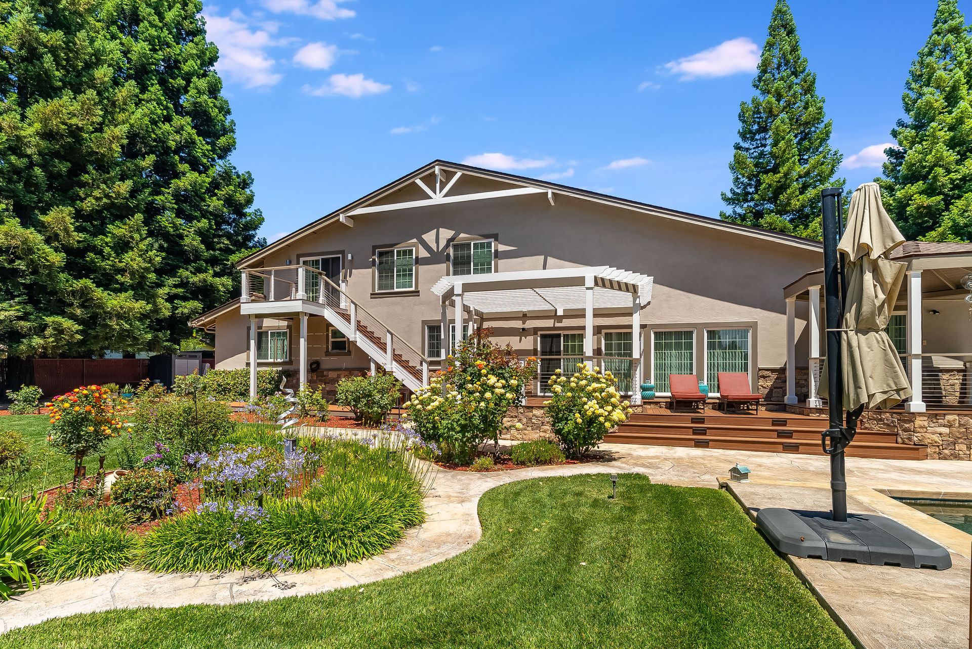Backyard patio with a two-story house, lush garden, and green lawn on a sunny day