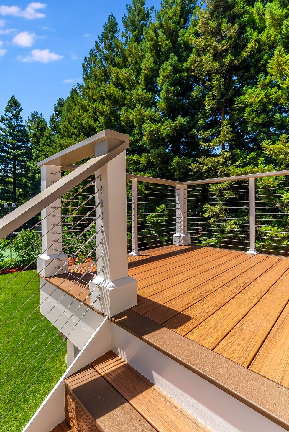 Wooden deck with white railing overlooking green trees and blue sky