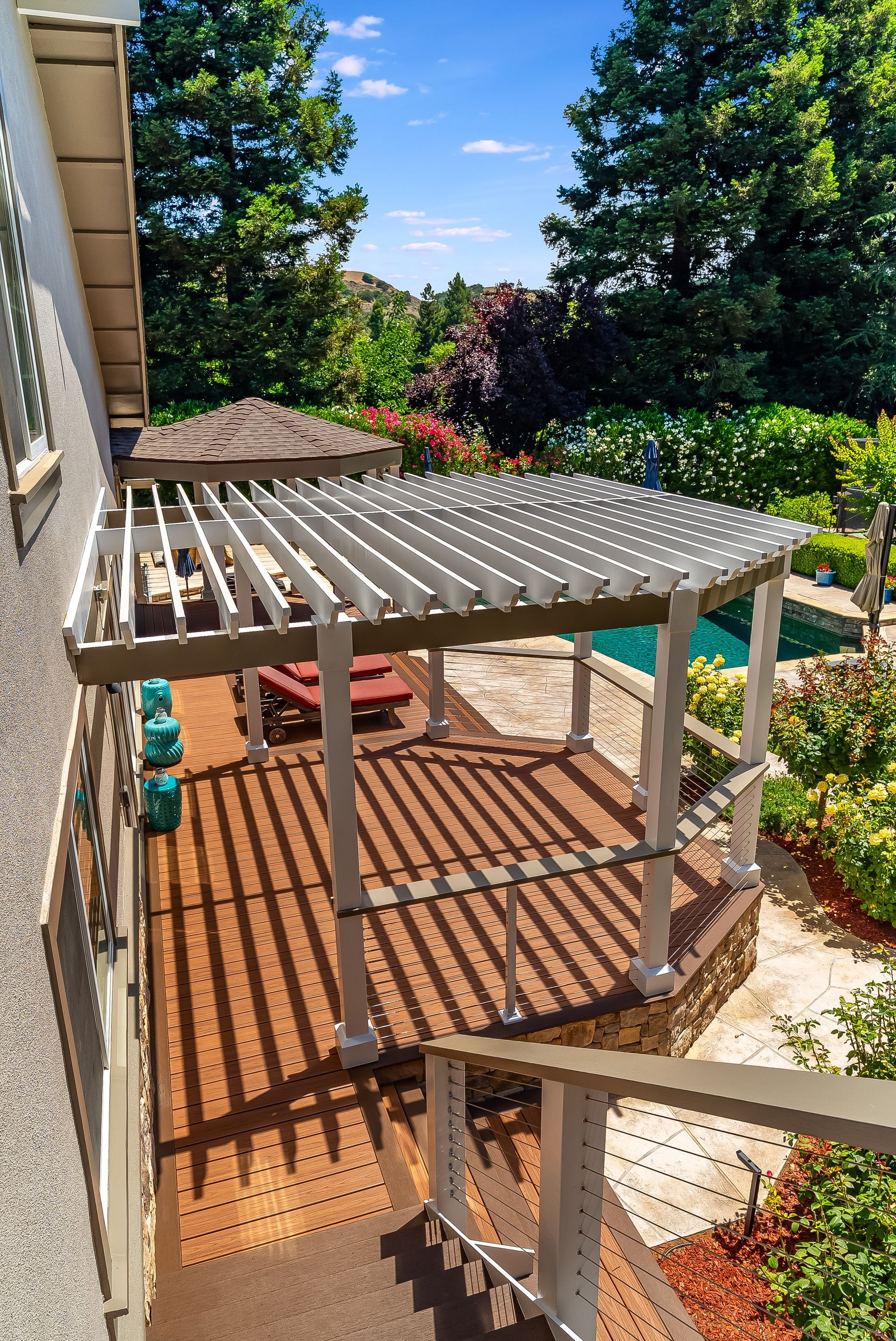 Back patio with gray pergola, deck stairs, and lush garden view in bright sunlight