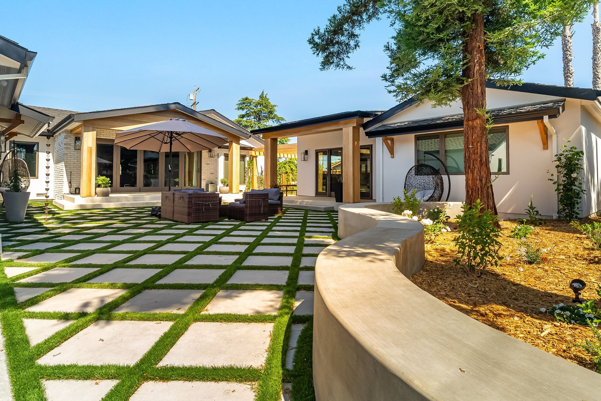 Modern courtyard with stone pavers, palm trees, and Mediterranean-style buildings under a clear blue sky