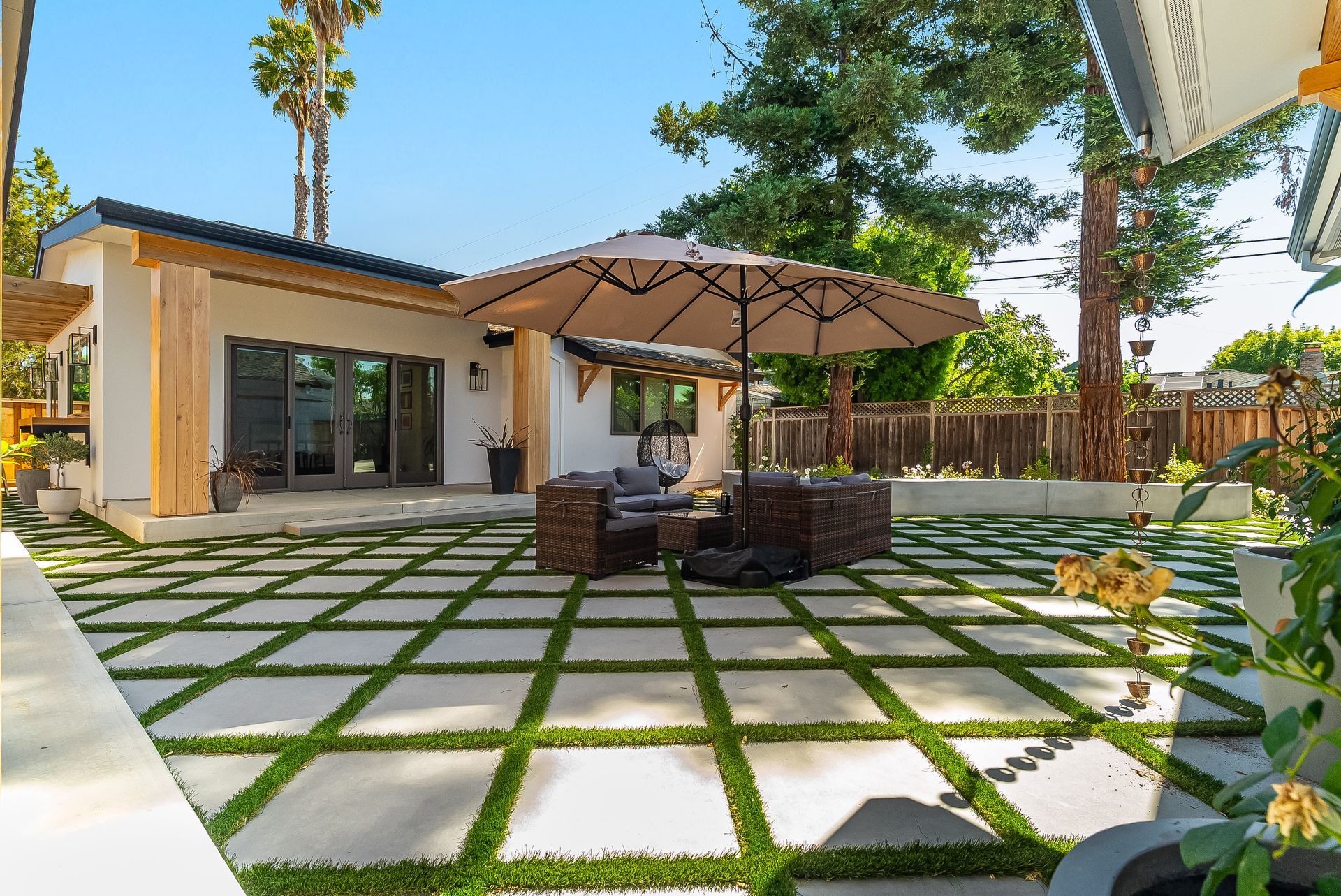 Modern patio with geometric pavers, outdoor sofa, umbrella, and sliding glass doors in a sunny backyard