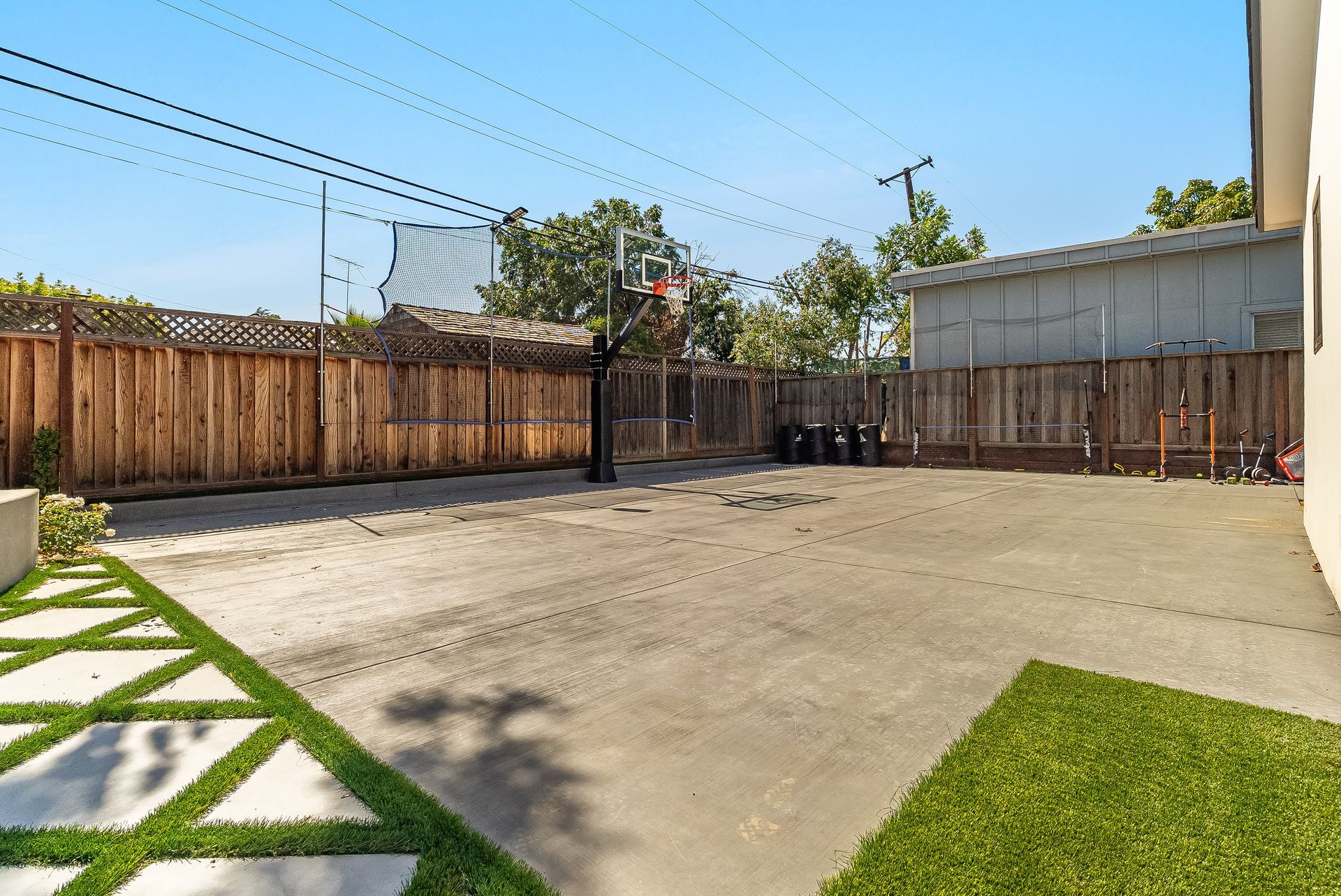 Empty backyard patio with concrete ground, grass edges, wooden fence, and blue sky