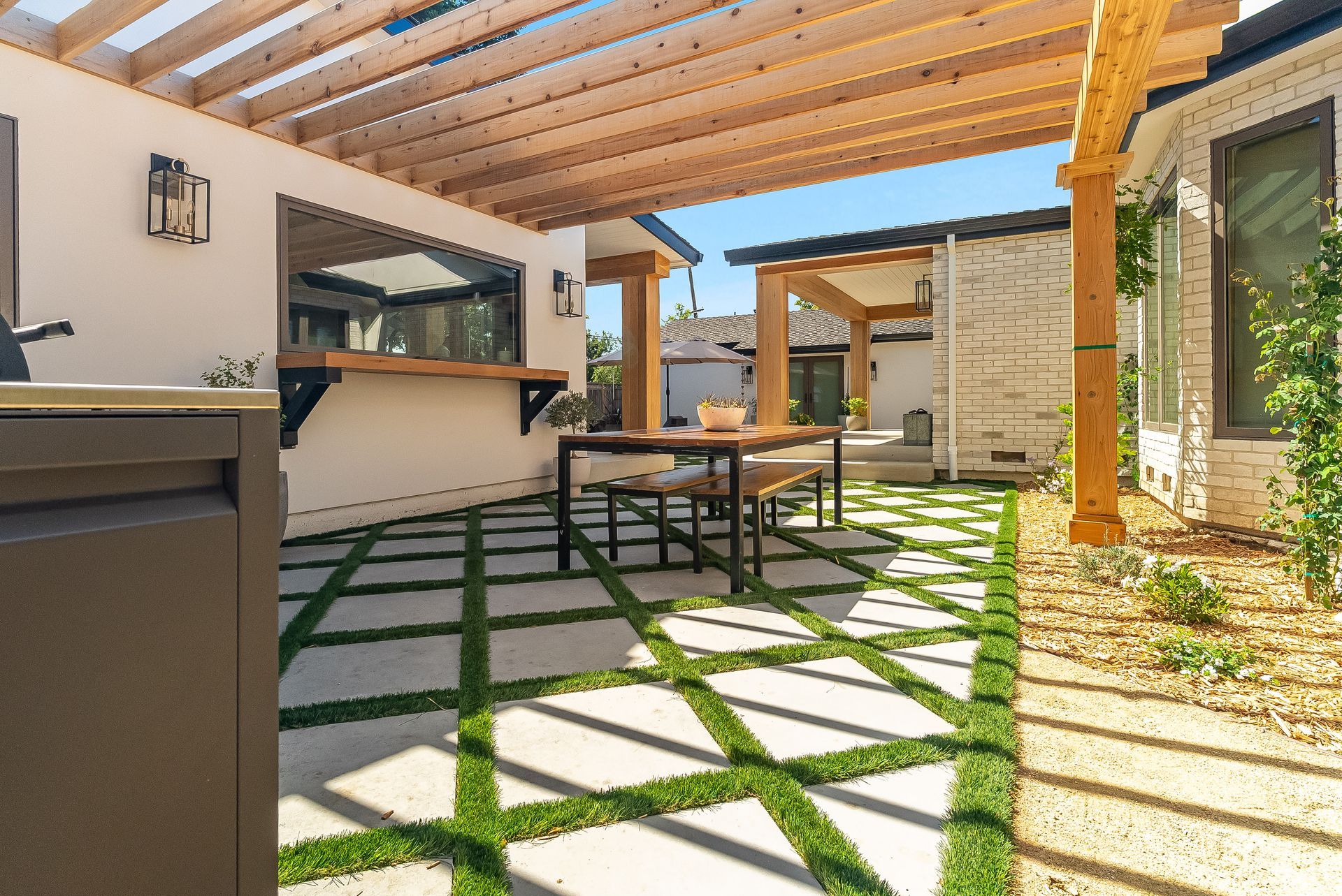 Covered patio with wood beams, stone pavers, and outdoor dining table beside a modern house