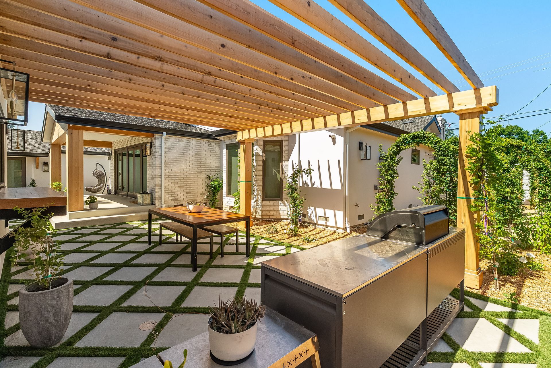 Covered patio with pergola, outdoor sofa, dining table, and potted plants in a bright courtyard
