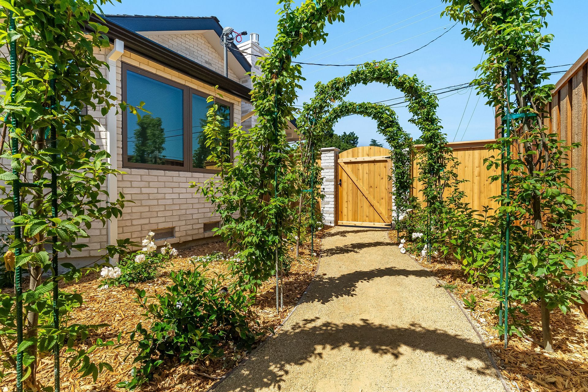Garden path leading to a wooden gate under a leafy arch beside a house