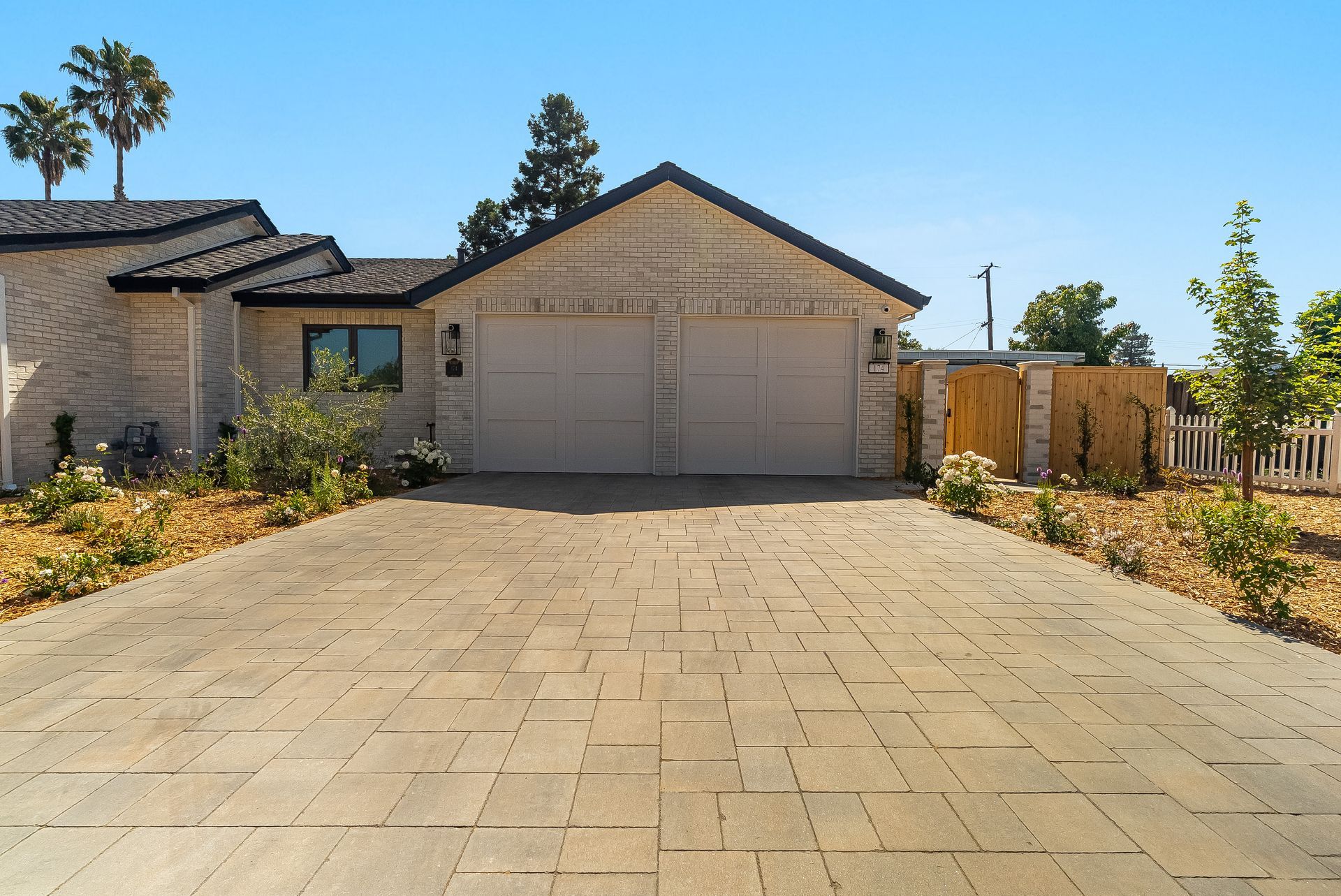 Single-story house with a wide paved driveway, two-car garage, and desert landscaping under a blue sky