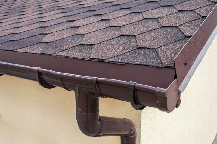 Brown roof edge with gutters and a downspout on a beige house
