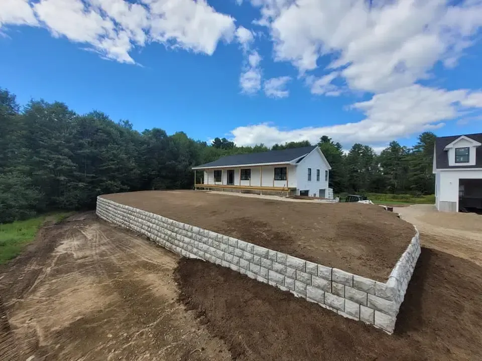 A house is sitting on top of a dirt hill next to a brick wall.