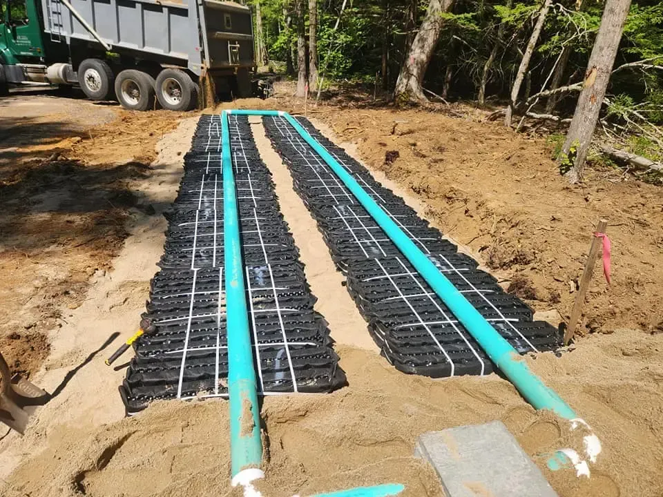 Construction site with septic system drain field installation. Green pipes and black grids laid in sandy ground.