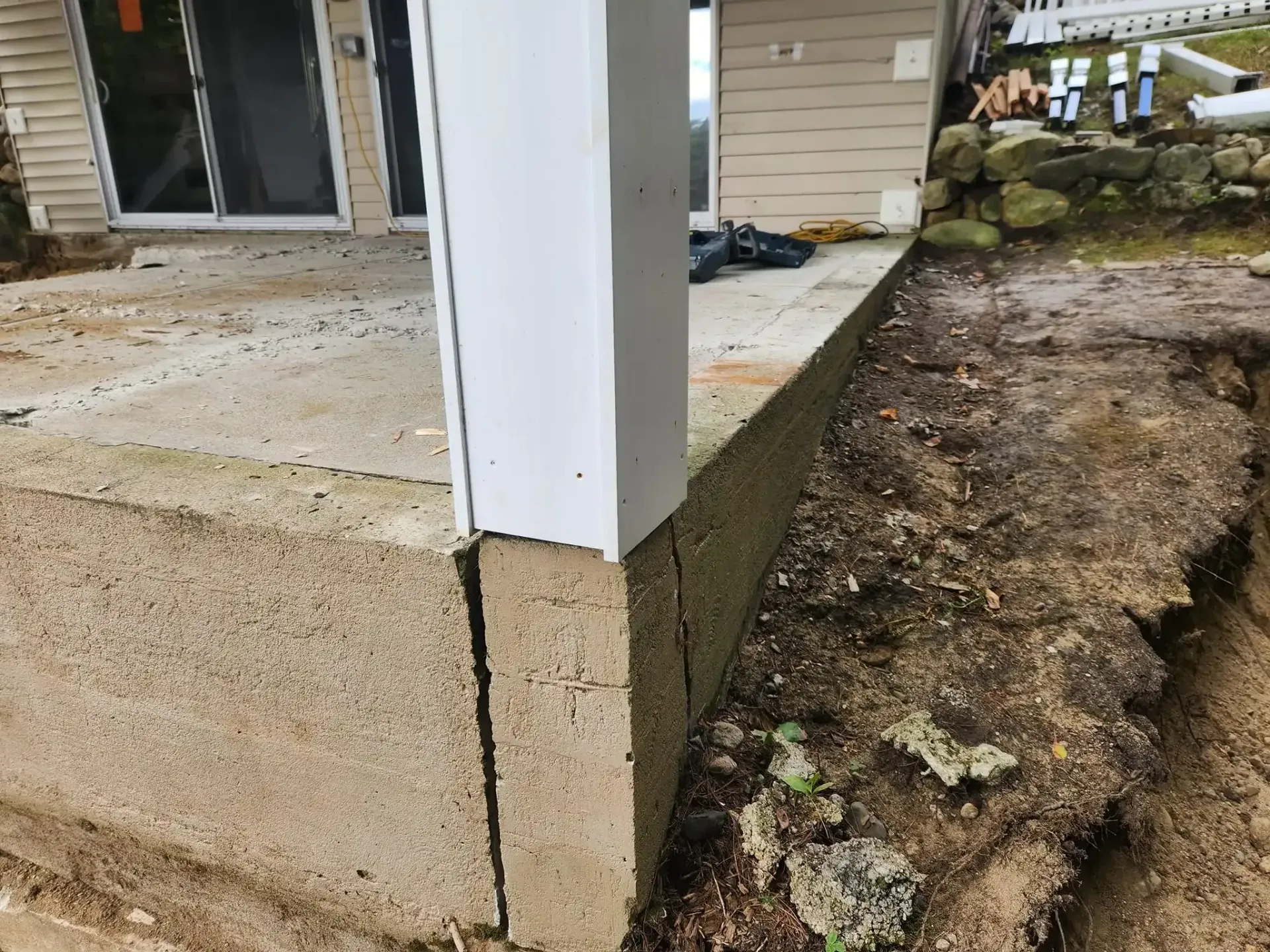 Concrete patio with cracked edge next to dirt and building support column.