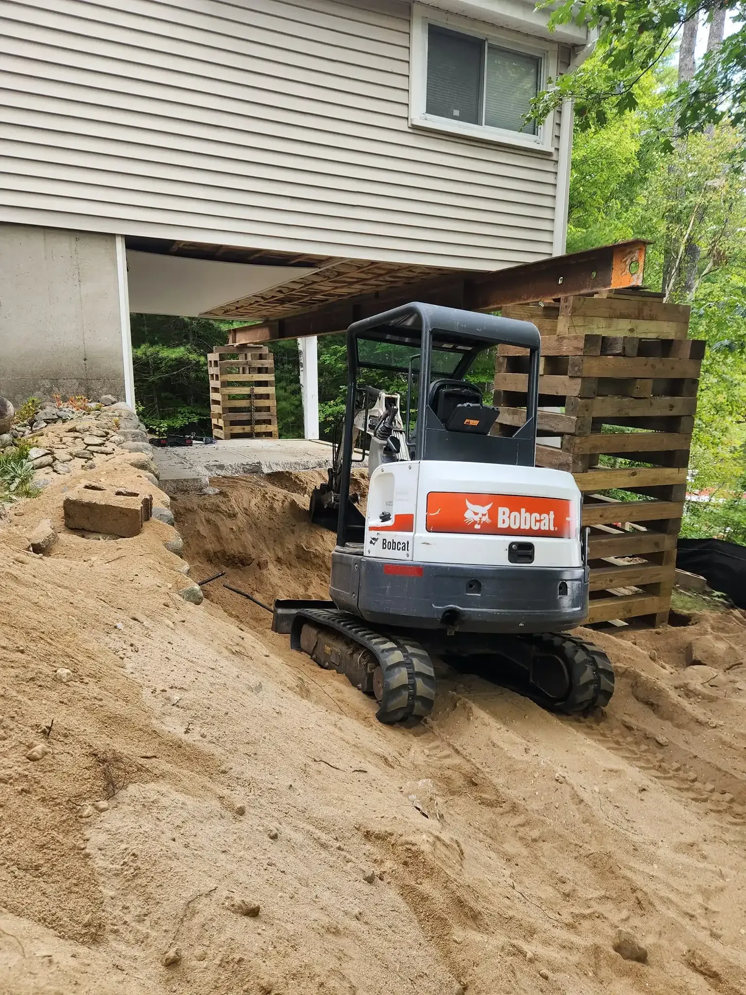 Bobcat excavator on a dirt slope near a house under construction.