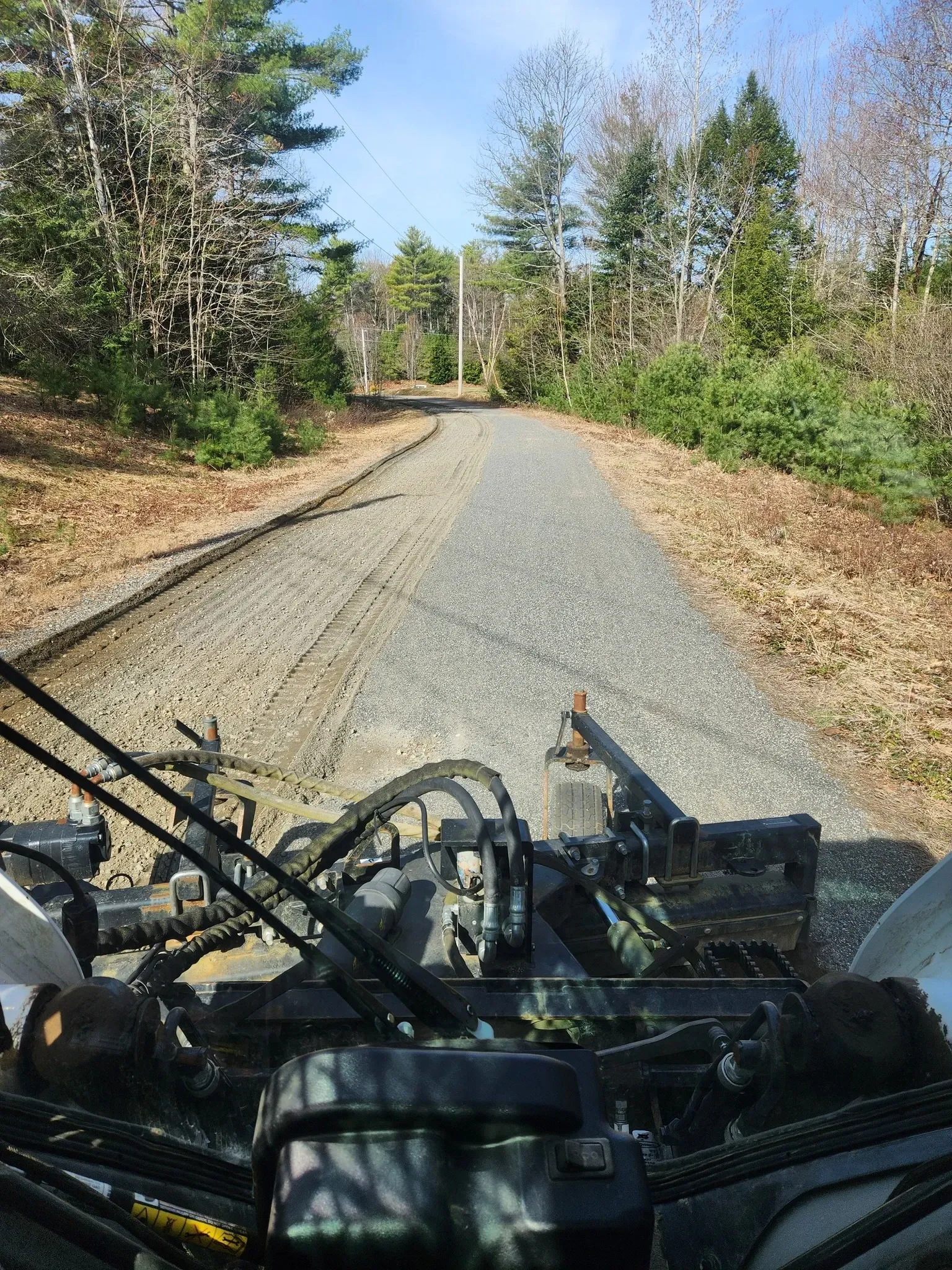 View from a vehicle traveling on a gravel path through a wooded area. The path extends into the distance.