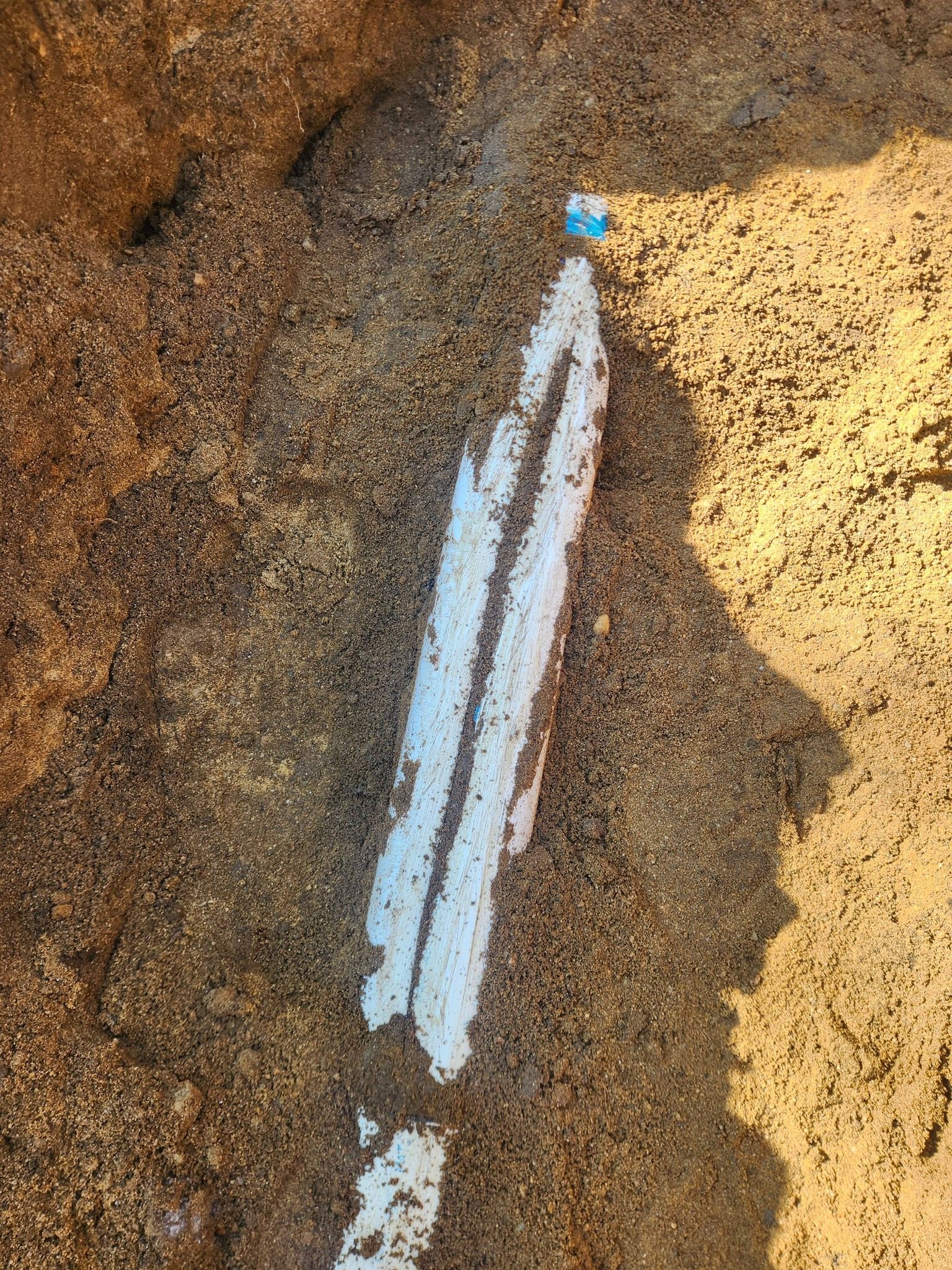 A straight white line painted on a textured, sandy ground surface, with a small blue marker at the top end.