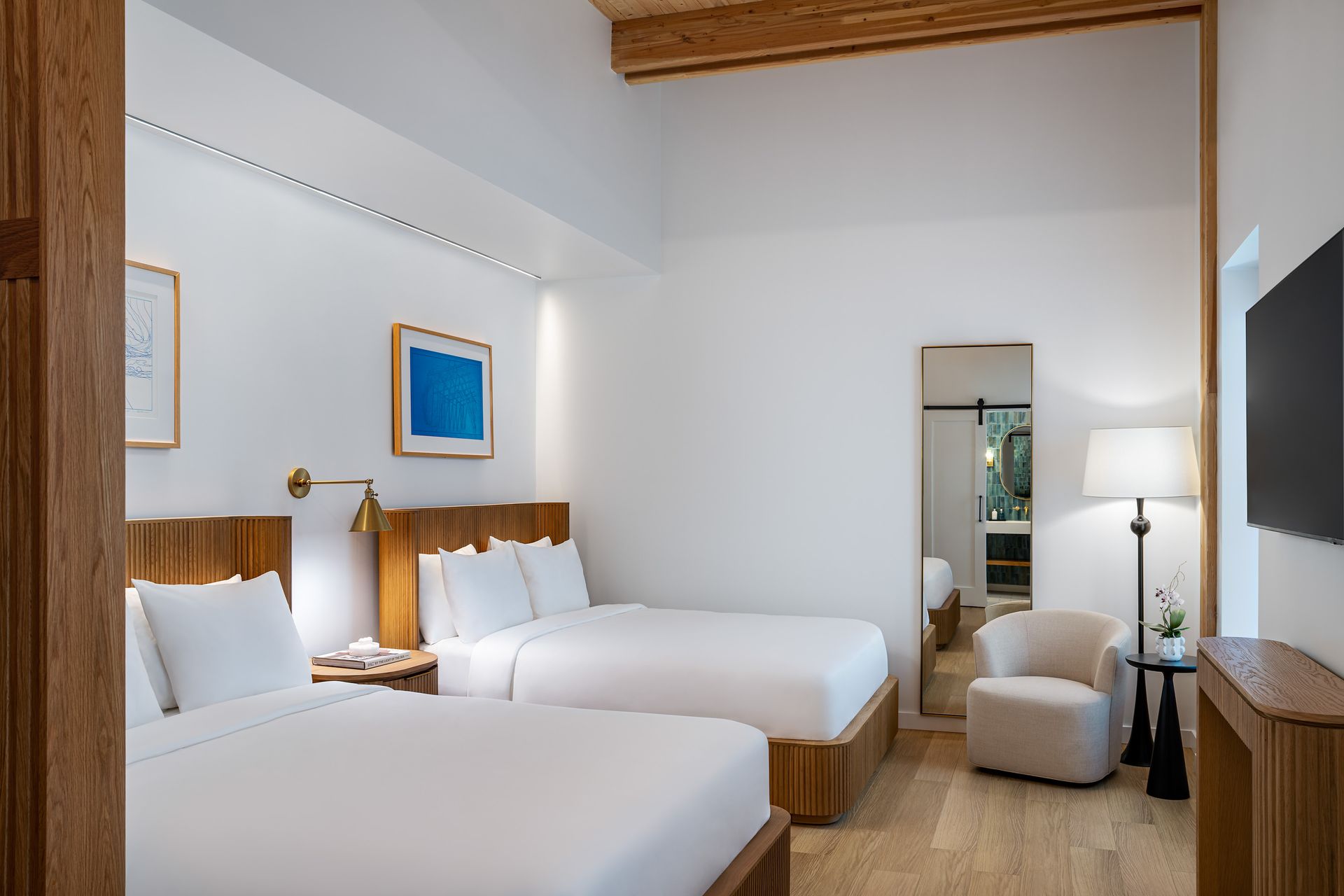 Minimalist hotel room with two beds, warm lighting, and a window seat