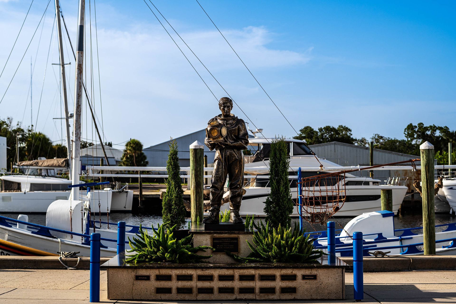Bronze statue holding helmet in front of historic diving boats
