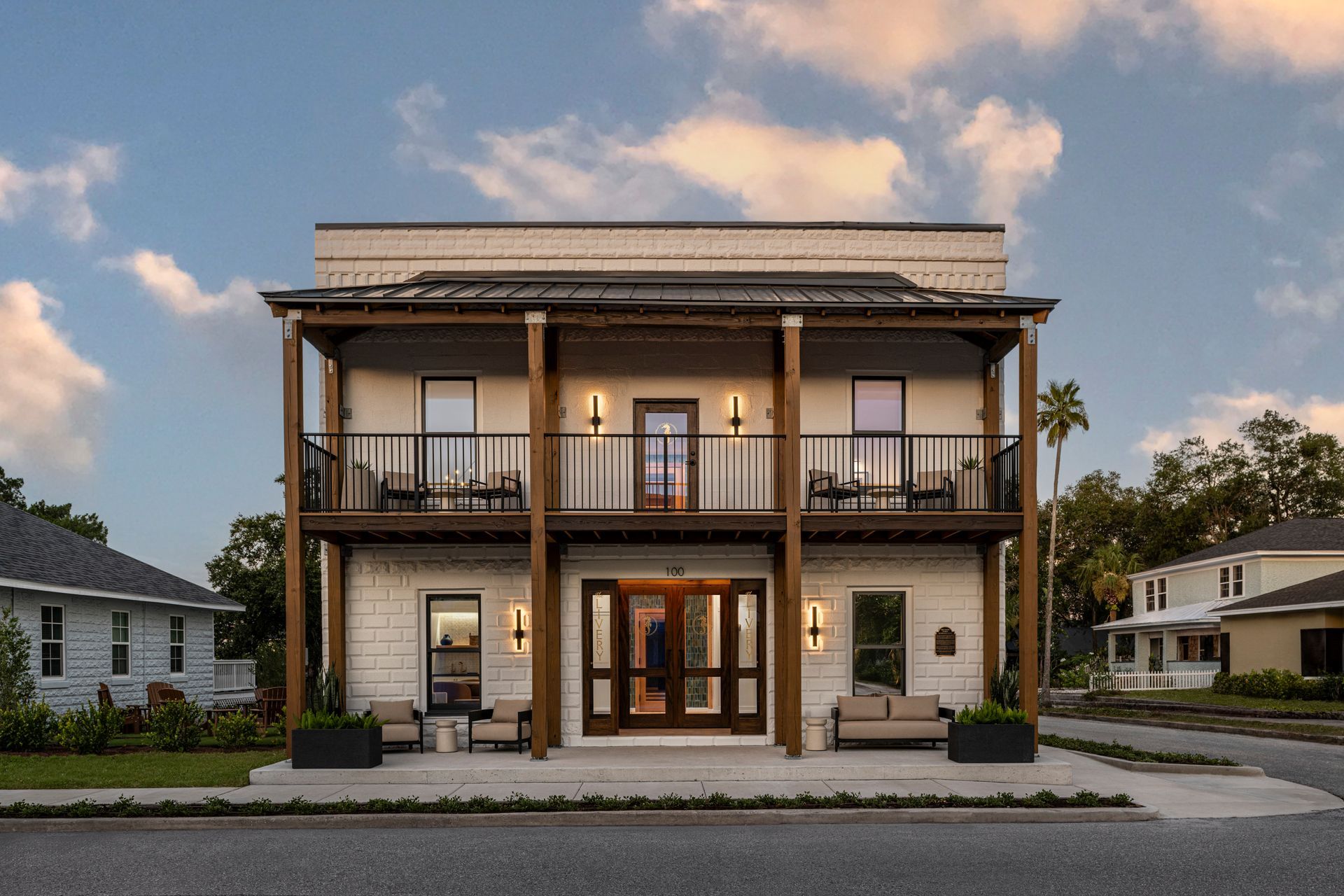 Two-story white building with a porch and balcony, palm trees, and ocean view.