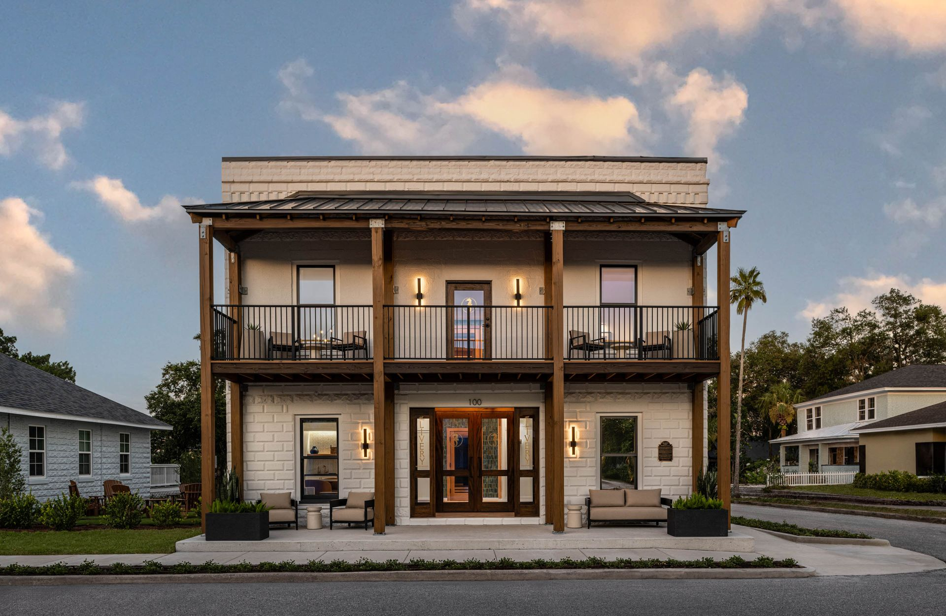 Two-story white building with a porch and balcony, palm trees, and ocean view.