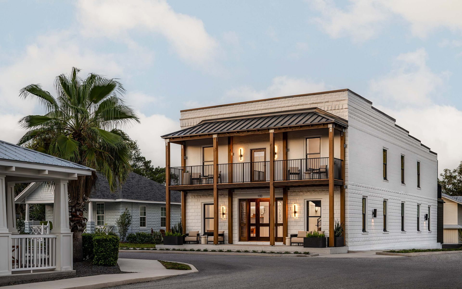 Two-story white building with wooden balcony and columns, beach setting. Person near the door.