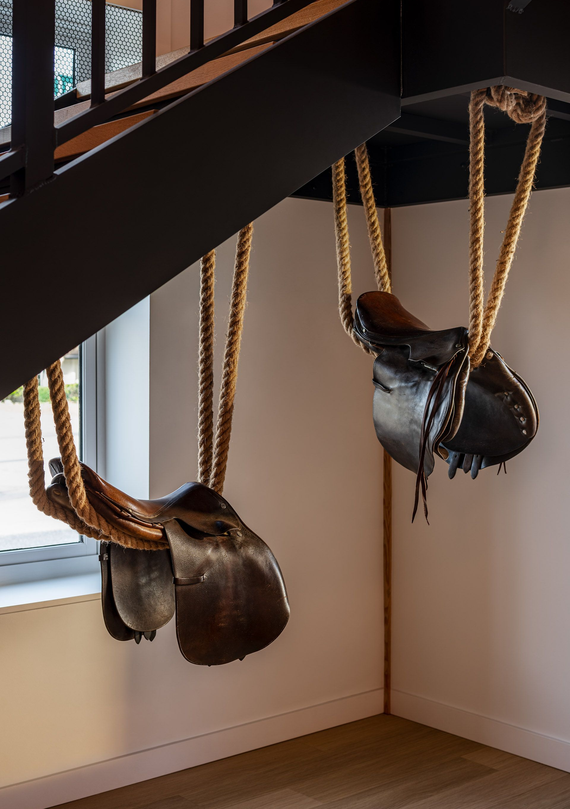 Two saddles handing on ropes inside under staircase