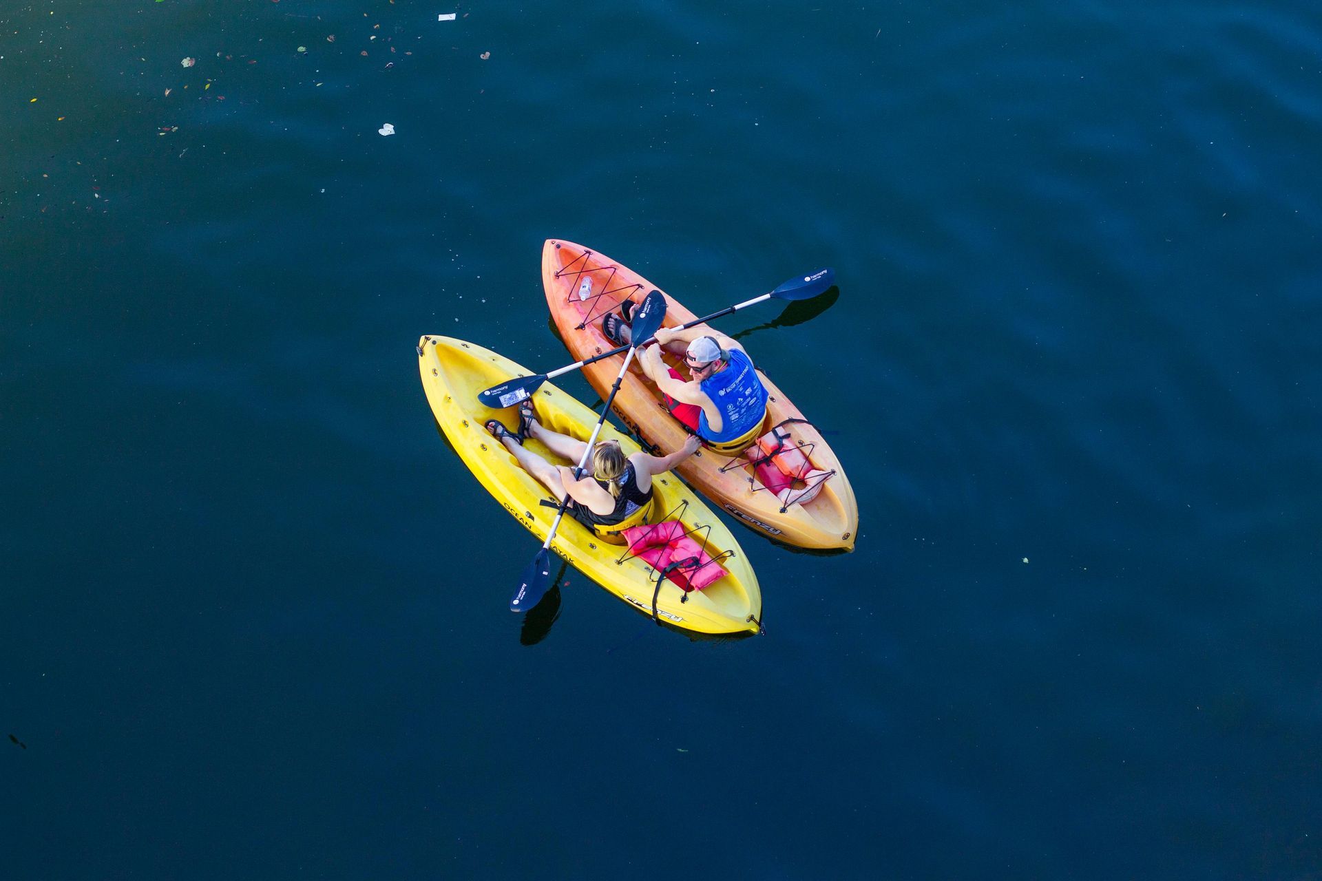 Two kayaks on dark blue water, one yellow, one orange. People are paddling.