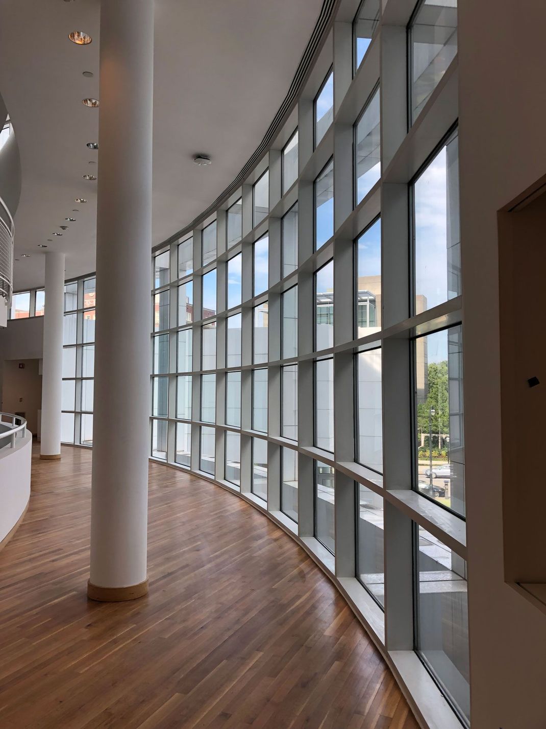Curved hallway with floor-to-ceiling windows, white columns, and polished wood floor