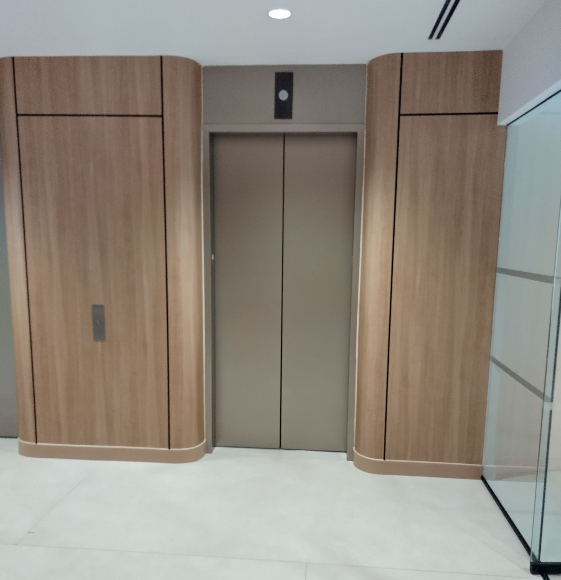 Wood-paneled elevator doors in a modern lobby with white tile flooring