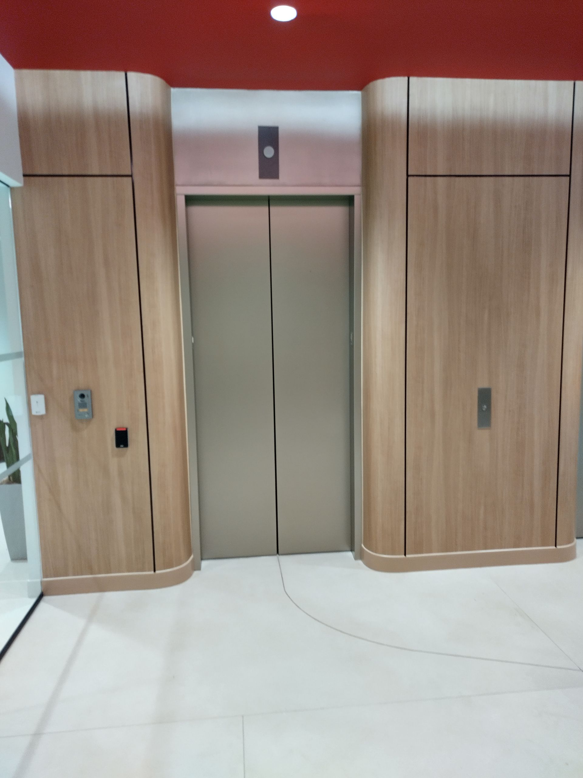 Modern elevator lobby with wood-paneled walls, closed elevator doors, and a curved white floor.
