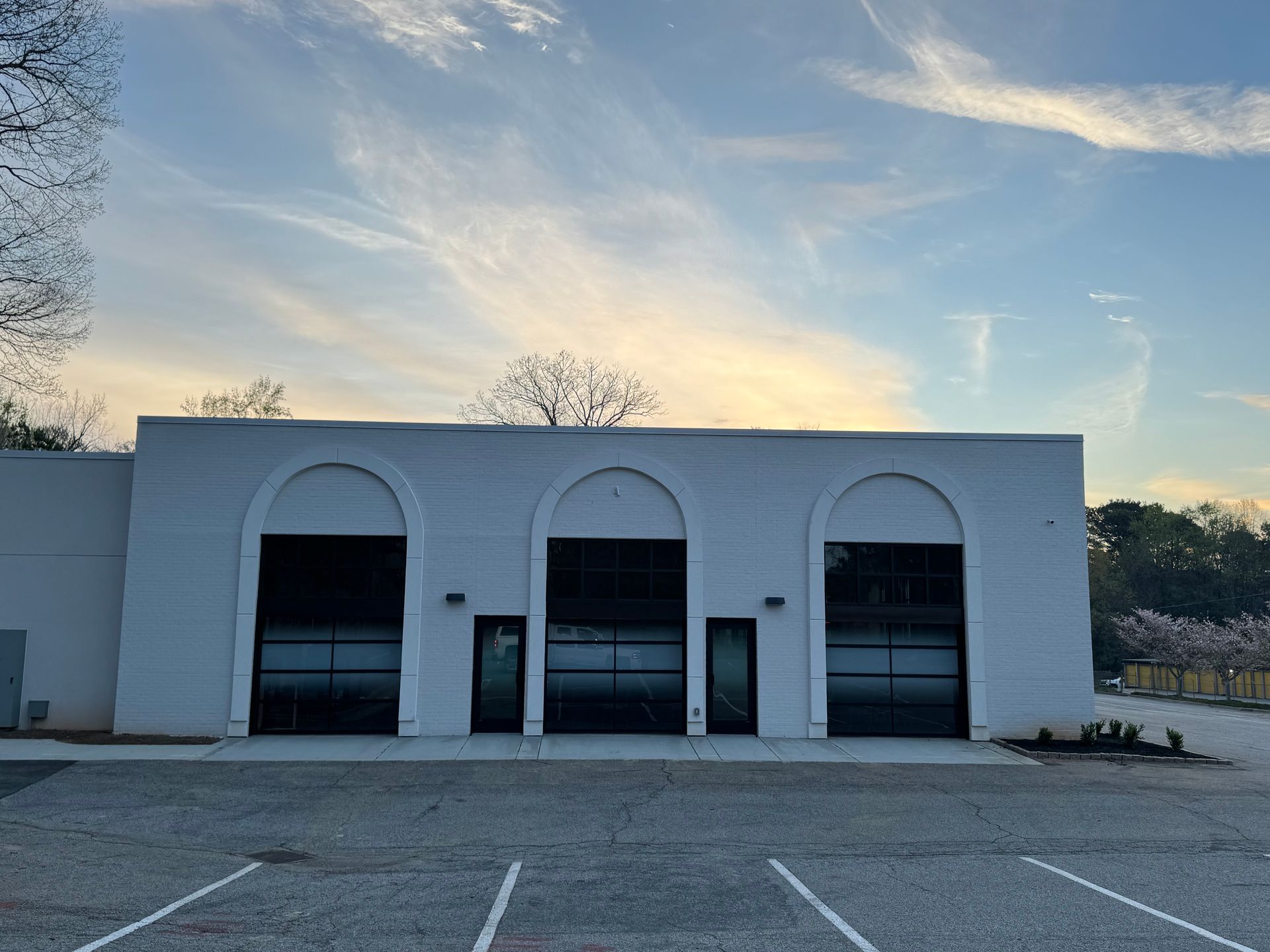 Empty white storefront with three arched doorways at dusk, seen from a parking lot
