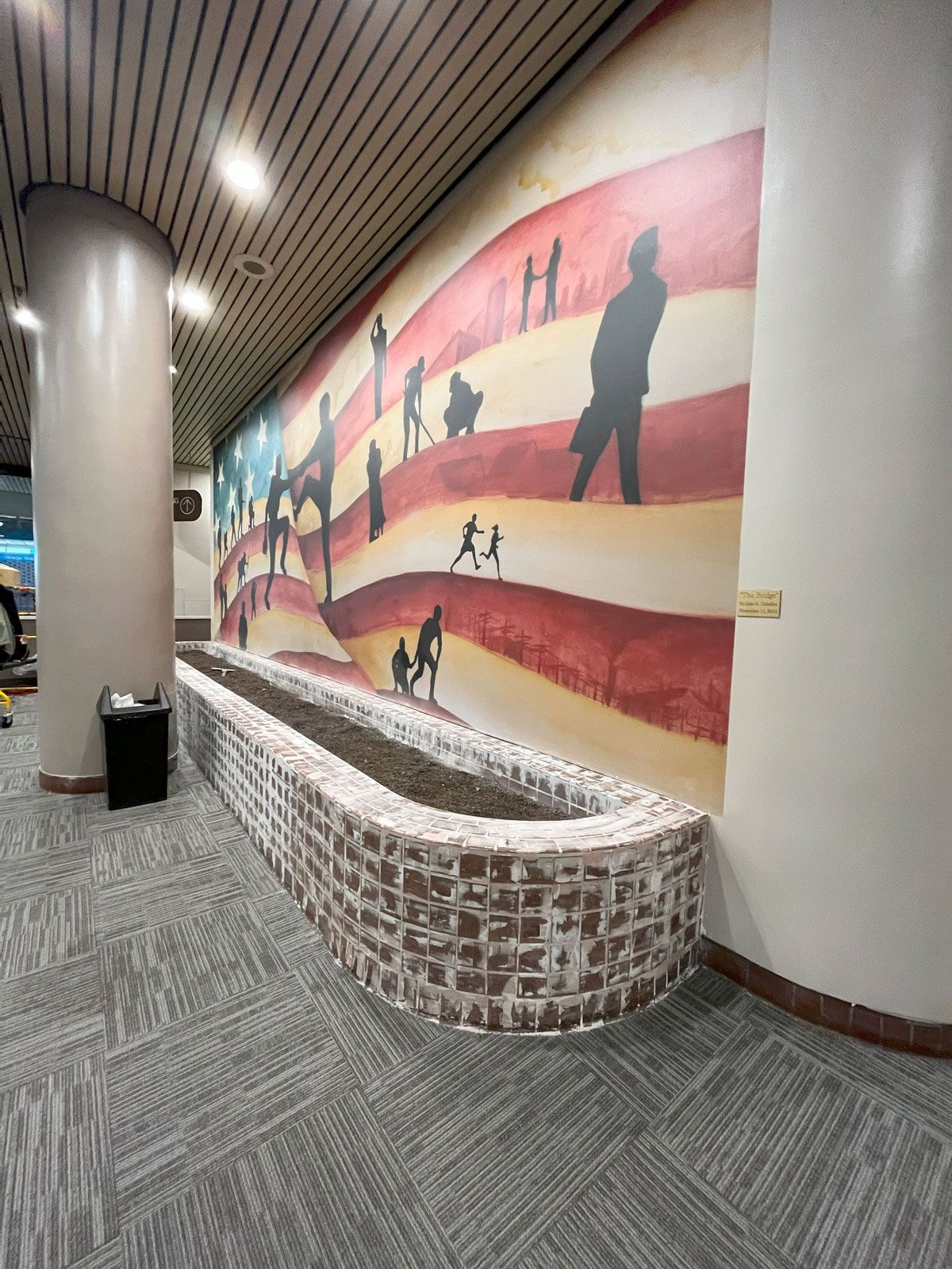 Curved bench beside a colorful wall mural in a carpeted indoor hallway