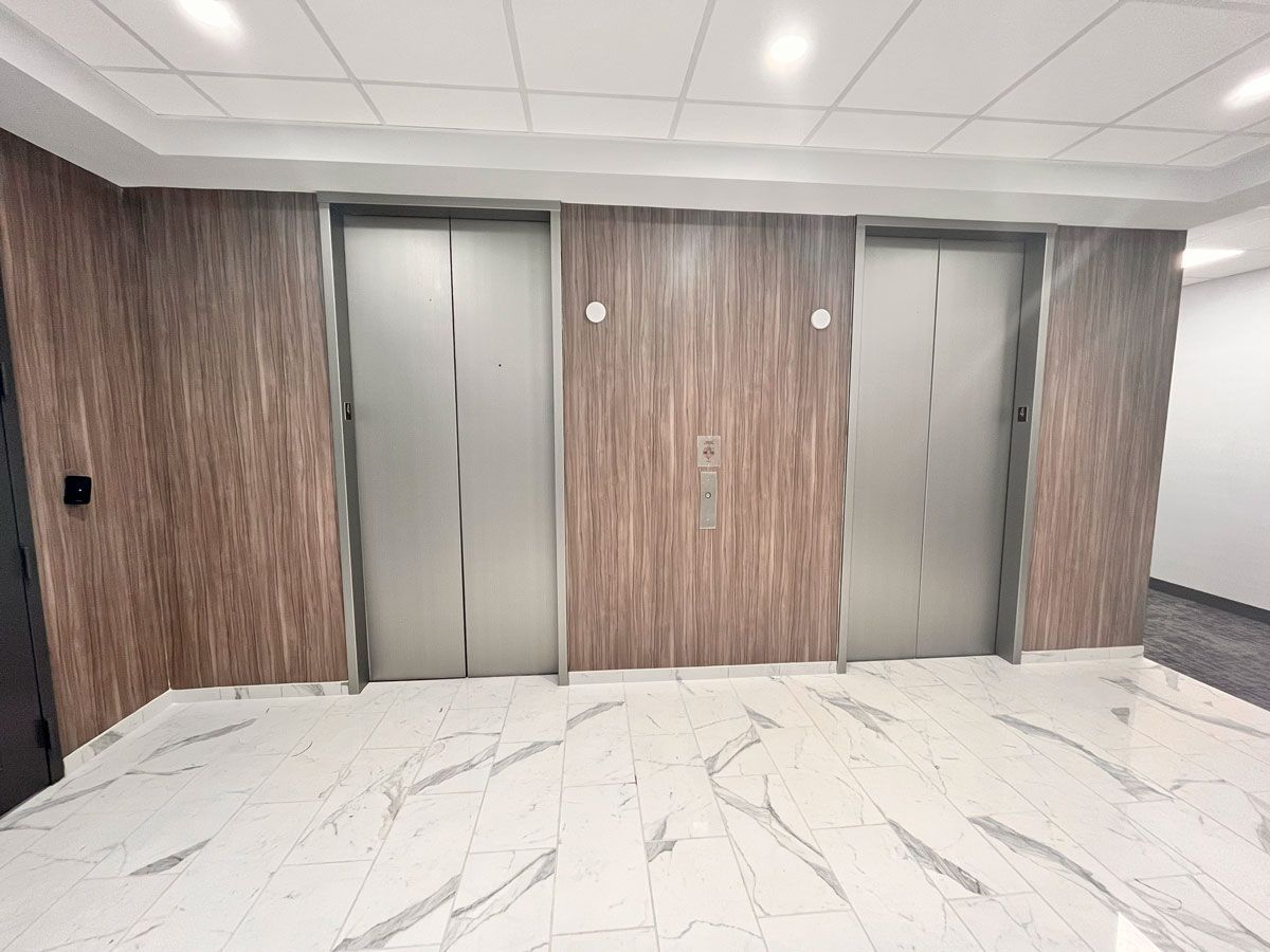 Office hallway with two closed elevators, wood-paneled walls, and a white marble-pattern floor