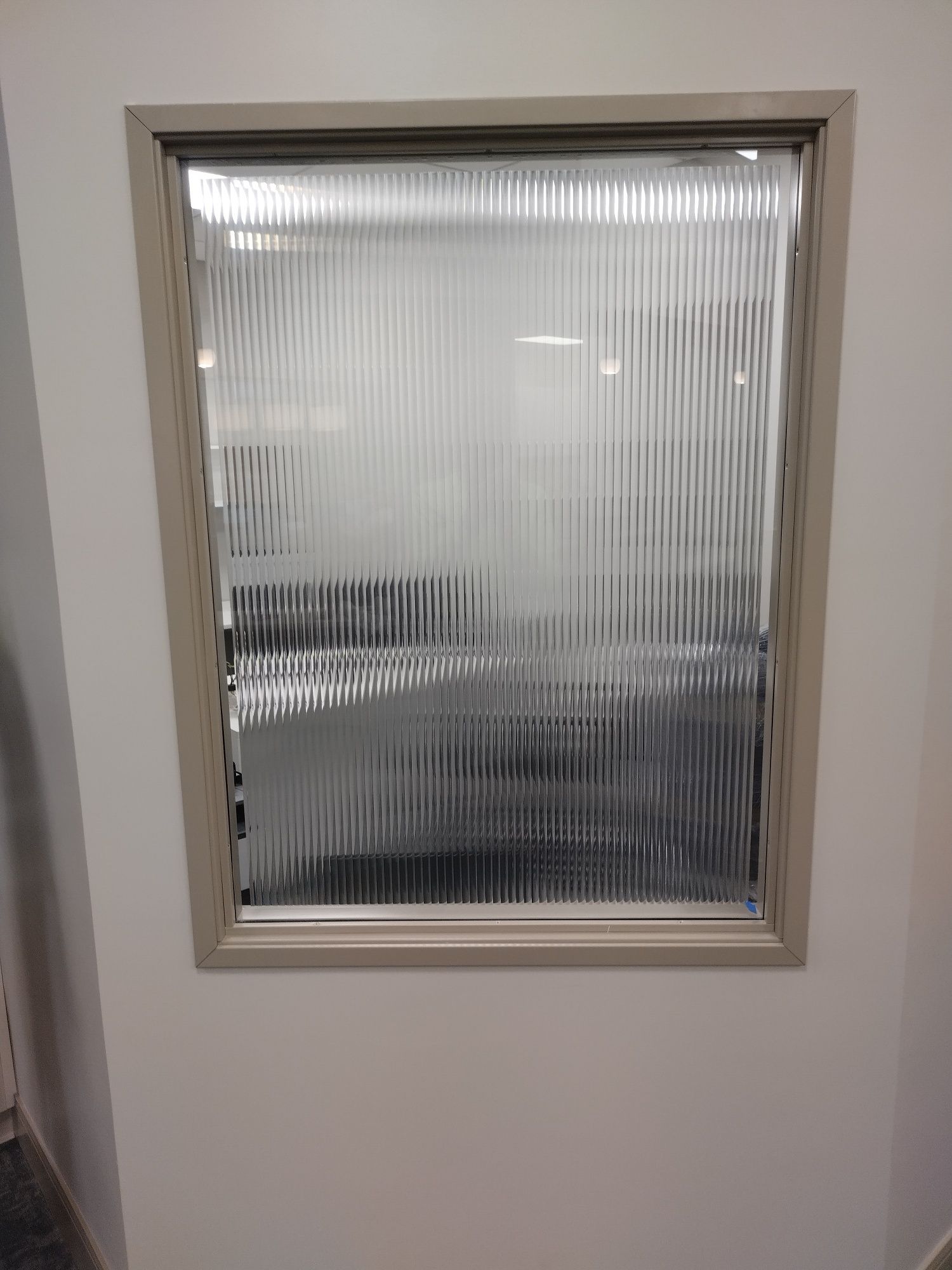 Small frosted glass window set in a beige wall, with vertical textured panes.