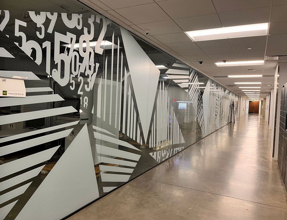 Empty office hallway with glass walls, geometric frosted designs, and overhead fluorescent lights